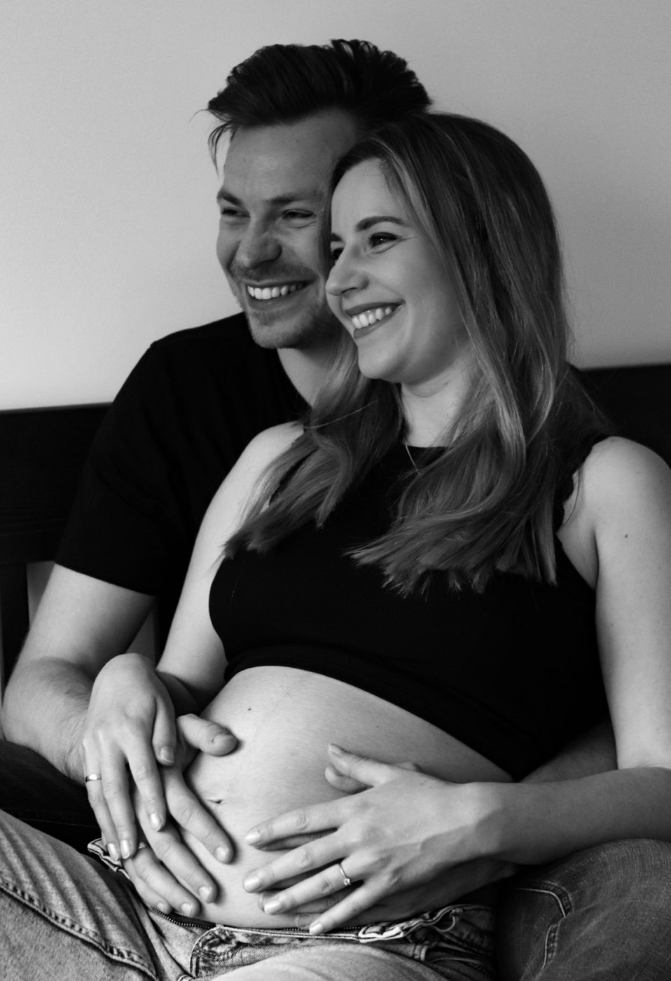 Schwarzweißaufnahme eines lachenden Paares, beide Hände auf dem Babybauch