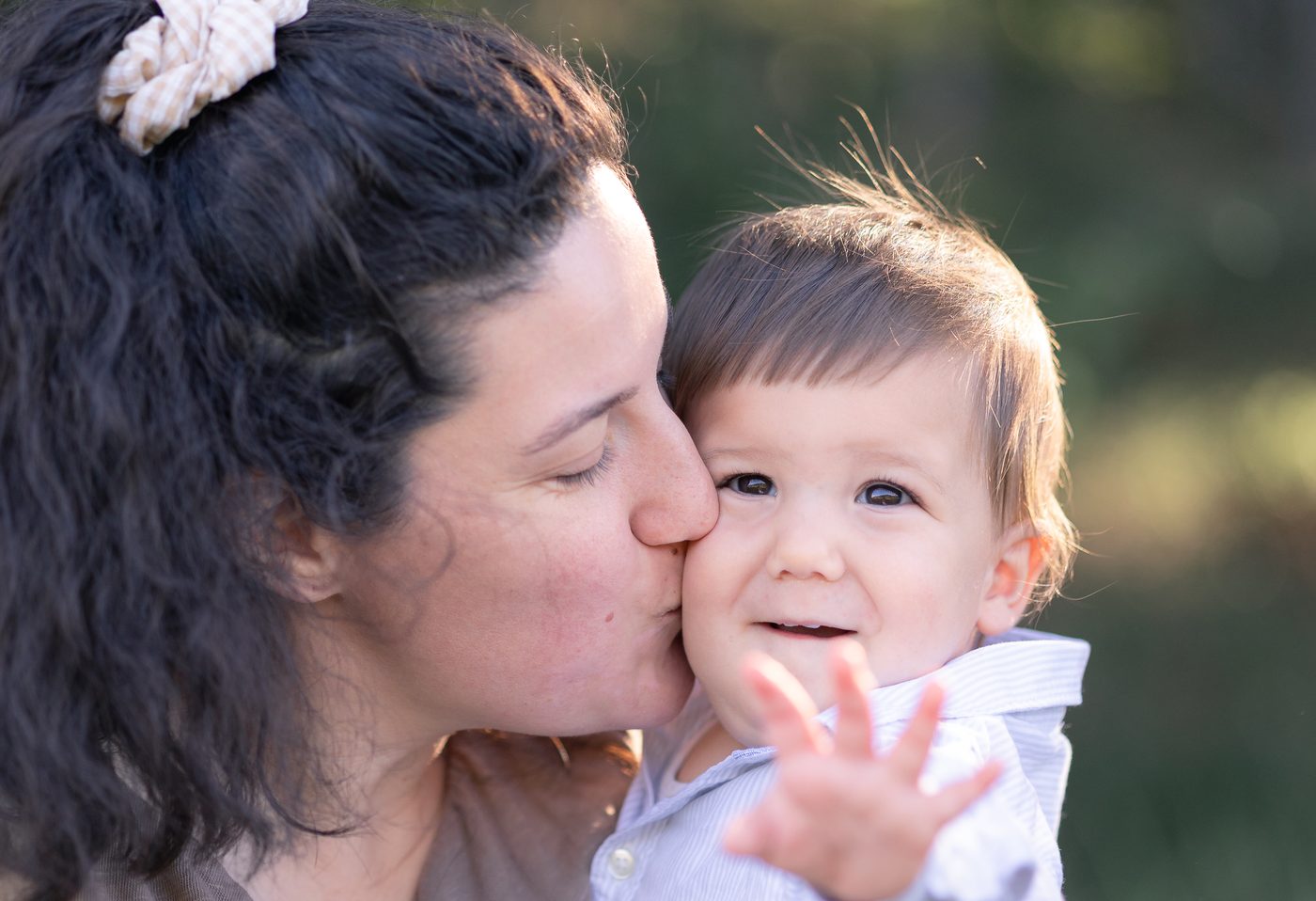 Eine Mama k&uuml;sst ihr lachendes Kleinkind, das in die Kamera winkt