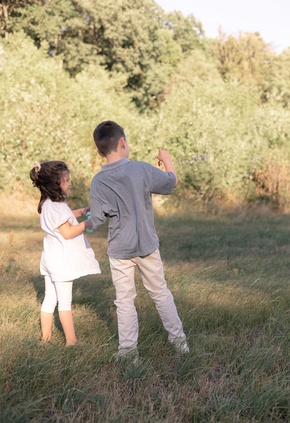 Zwei Geschwister spazieren in der Abendsonne &uuml;ber die Wiese