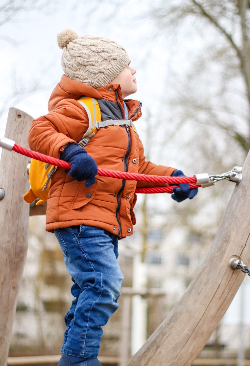 Der Bub balanciert auf dem Spielplatz und h&auml;lt sich an einem roten Seil fest