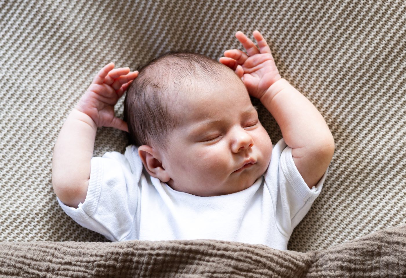 Ein schlafendes Baby hat beide &Auml;rmchen &uuml;ber den Kopf gestreckt