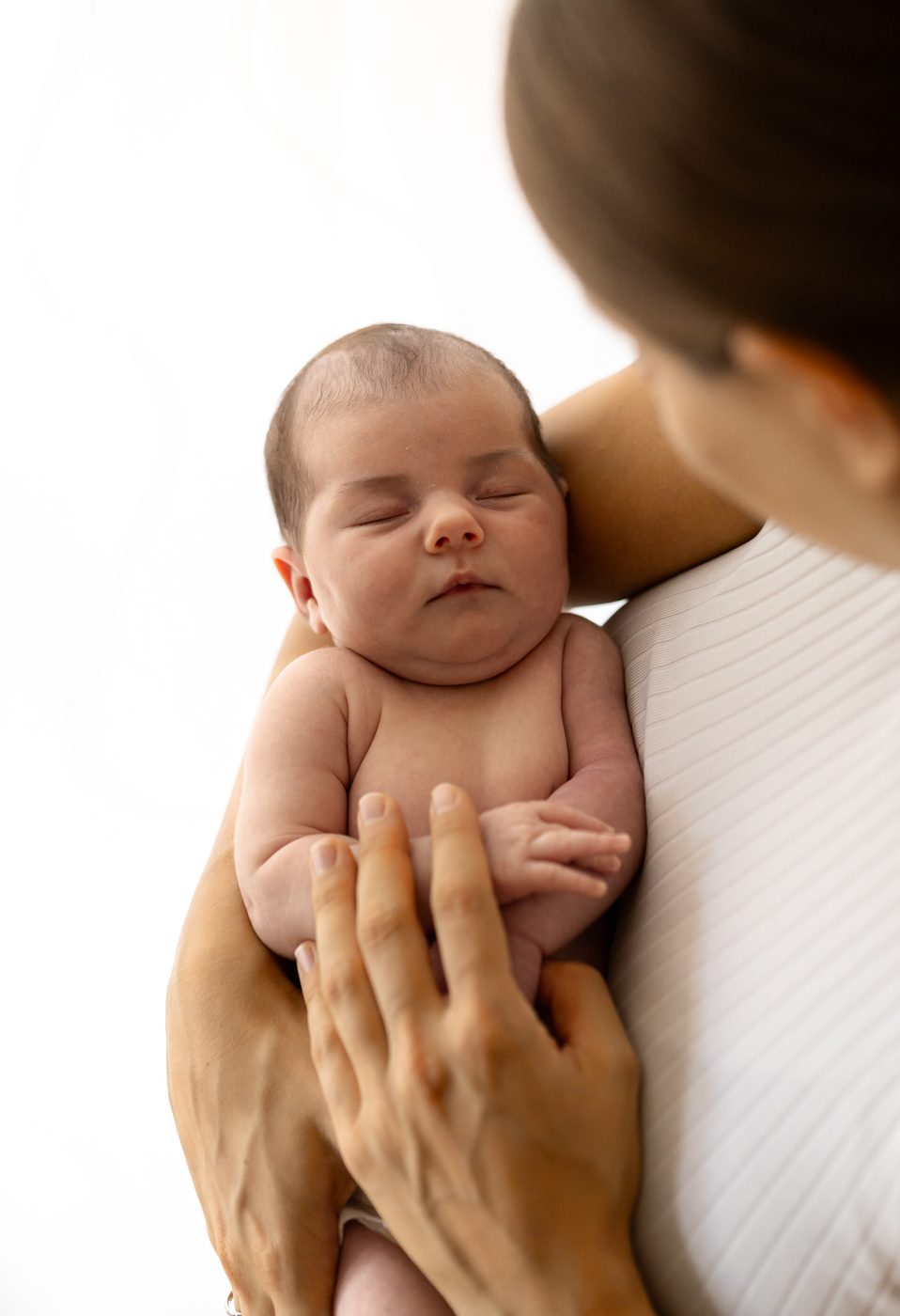 Ein Neugeborenes liegt an der Schulter seiner Mama, sie h&auml;lt es mit beiden H&auml;nden