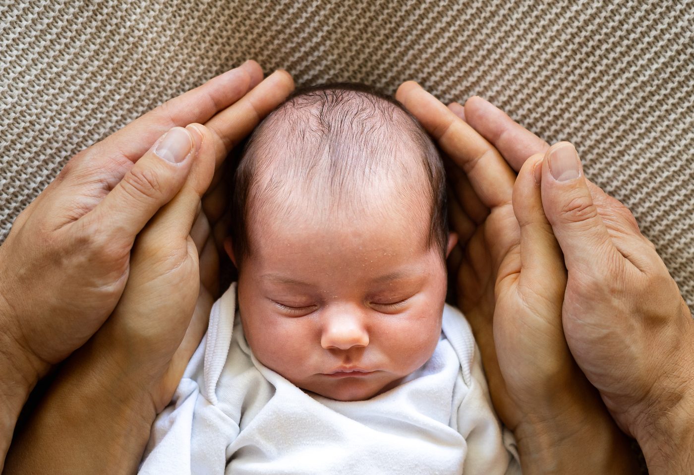 Die H&auml;nde der Eltern umrahmen den Kopf des schlafenden Babys