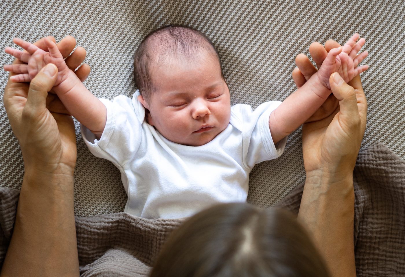 Die Eltern halten die winzigen H&auml;nde ihres schlafenden Babys