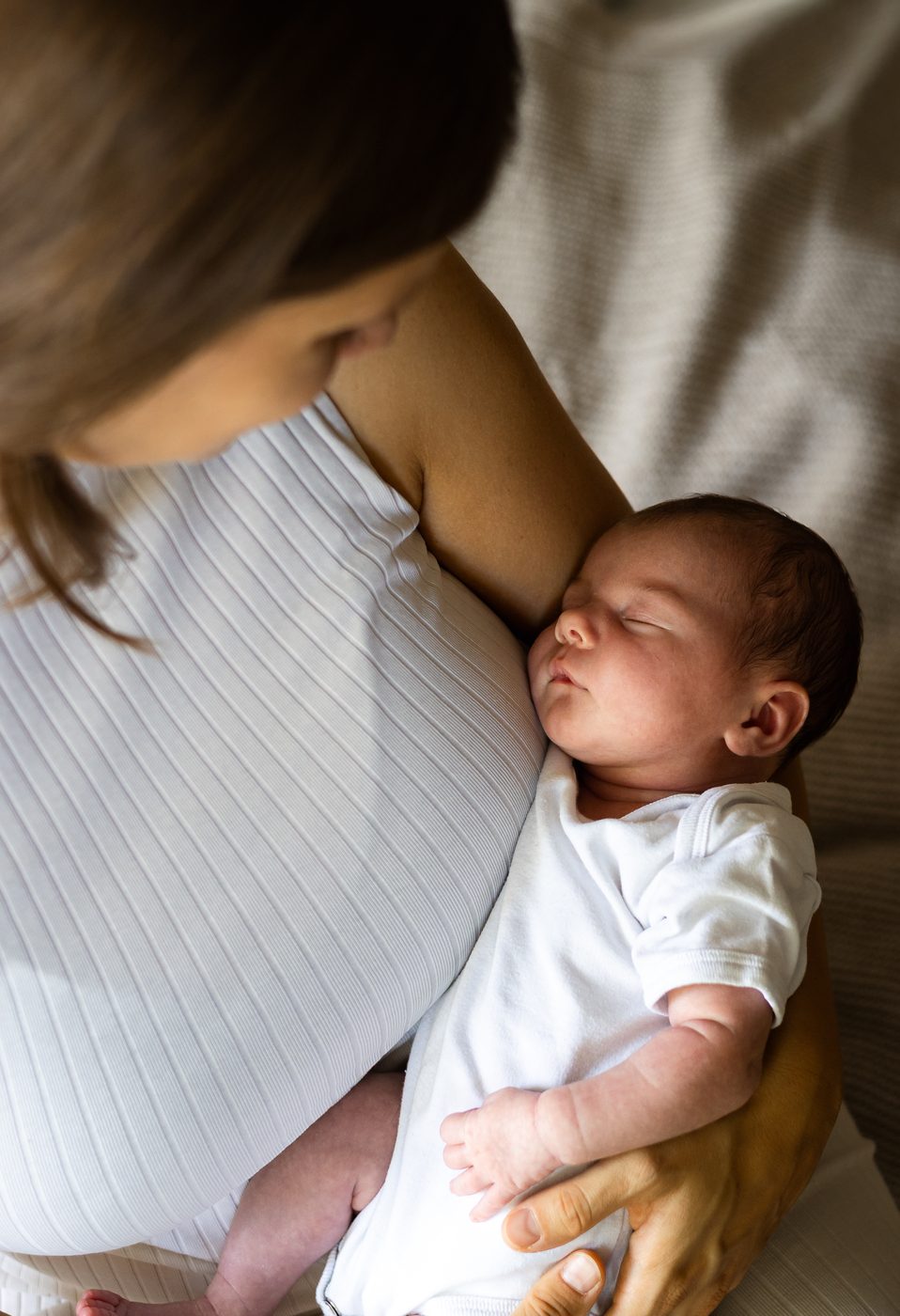 Von oben gesehen: ein Baby schmiegt sich im Arm seiner Mama an sie