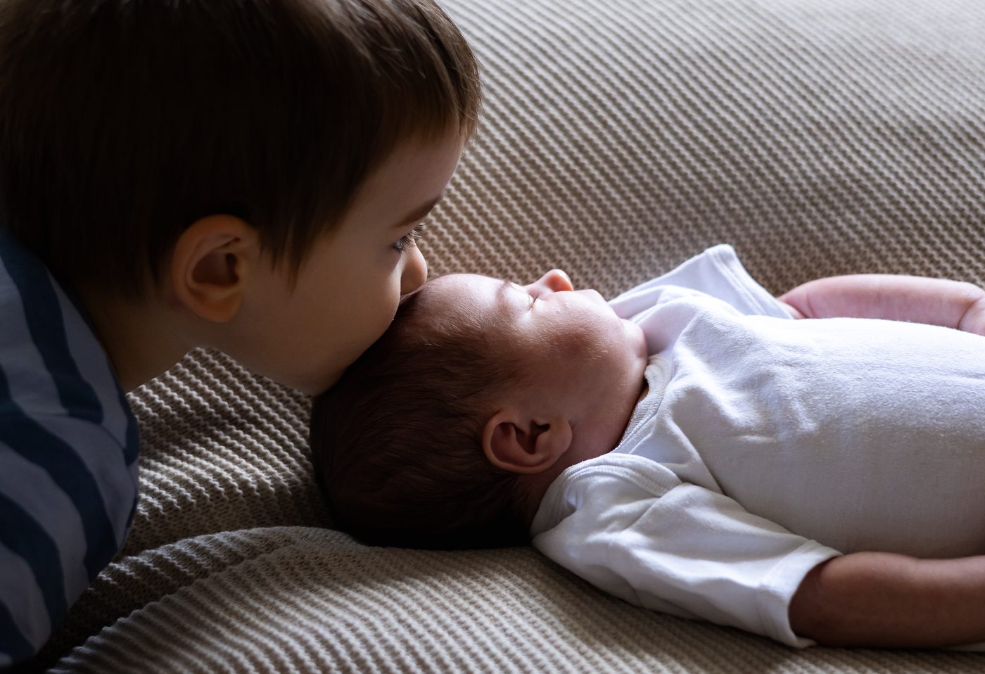 Ein gro&szlig;er Bruder gibt dem schlafenden Baby einen Kuss auf den Kopf