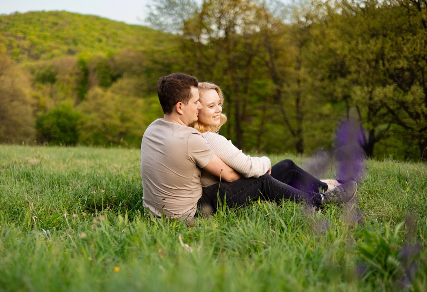 Ein Paar sitzt umschlungen im Gras und blickt in die Landschaft